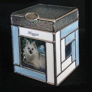 May include: A blue and white stained glass box with a photo of a white dog and the name "Maggie" on the front.