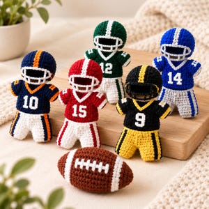 May include: Five small crochet figures dressed in football uniforms with helmets and jerseys numbered 10, 15, 12, 9, and 14, arranged with a brown and white crochet football. The figures feature various color combinations including navy, red, green, black, and blue.