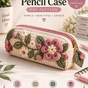 May include: A crochet pencil case featuring a cream-colored base with decorative pink flowers and green leaves. The case has a pink zipper closure with a matching leaf-shaped pull. Text on the image includes Crochet Pencil Case PDF Pattern.
