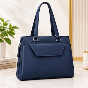 May include: A structured navy blue handbag featuring two vertical handles, a front flap pocket with a triangular edge, and silver-toned metal hardware. The bag has a smooth finish and a rectangular base, with a side zipper pull visible on the left.