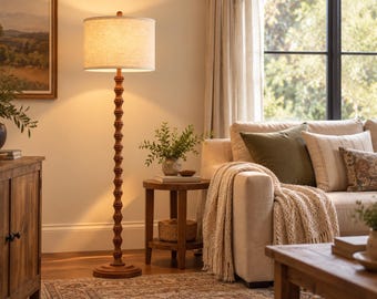 May include: A floor lamp with a tall, slender, turned wooden post featuring a series of stacked, rounded decorative beads. The lamp is topped with a cylindrical, off-white fabric drum shade that emits a warm, soft glow.