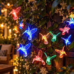 Pode incluir: Uma corrente de luzes LED decorativas com coberturas translúcidas em forma de beija-flor em cores vibrantes, incluindo vermelho, azul, verde e laranja. Os pássaros estão presos a um fio escuro e emitem um brilho intenso para iluminação festiva.