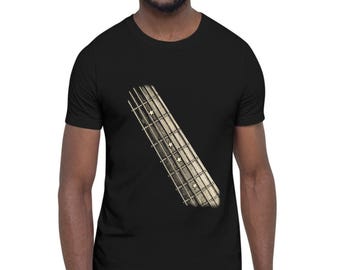 May include: A black short-sleeved t-shirt featuring a graphic print of a guitar fretboard positioned diagonally across the chest. The fretboard design includes small star-shaped inlays along the neck, rendered in a vintage, weathered aesthetic.