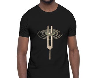 May include: A black short-sleeve t-shirt featuring a graphic print of a metallic tuning fork in the center. The tuning fork is depicted in a light beige tone with concentric circular ripples emanating from the top, creating a visual effect of sound waves.