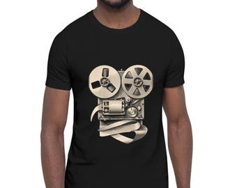 May include: A black short-sleeved t-shirt featuring a graphic print of a vintage reel-to-reel tape recorder in shades of grey and cream. The illustration depicts the mechanical reels, tape path, and central motor housing centered on the chest area.
