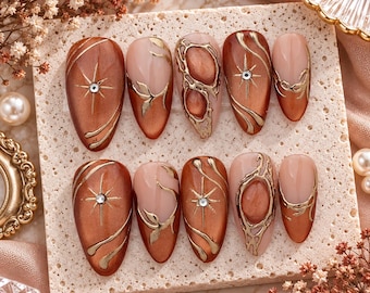 Unhas postiças artesanais em tom marrom cobre, com arte abstrata em cromo dourado e design de estrela celestial (formato amendoado).