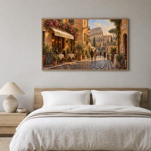 Puede incluir: Una impresión de arte mural enmarcada que representa una escena callejera romana con un café llamado Caffe Roma, mesas al aire libre y el Coliseo al fondo. La escena presenta iluminación cálida, calles empedradas y personas caminando.