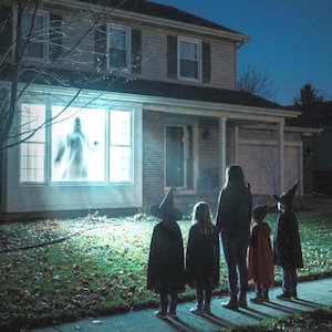 May include: A two-story house at night with a glowing white ghost projection visible in the large front window. Four figures stand on the lawn in front of the house, wearing dark capes and pointed hats, looking toward the illuminated window.