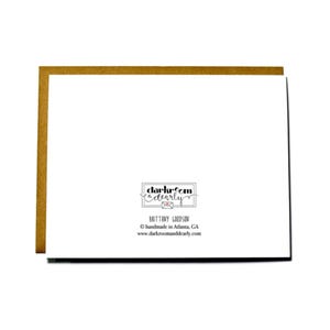 May include: A white card with black text that reads "darkroom & dearly" with a small red heart and the text "BRITTANY GOODSON" below. The text "handmade in Atlanta, GA" and "www.darkroomanddearly.com" are also included in black text.