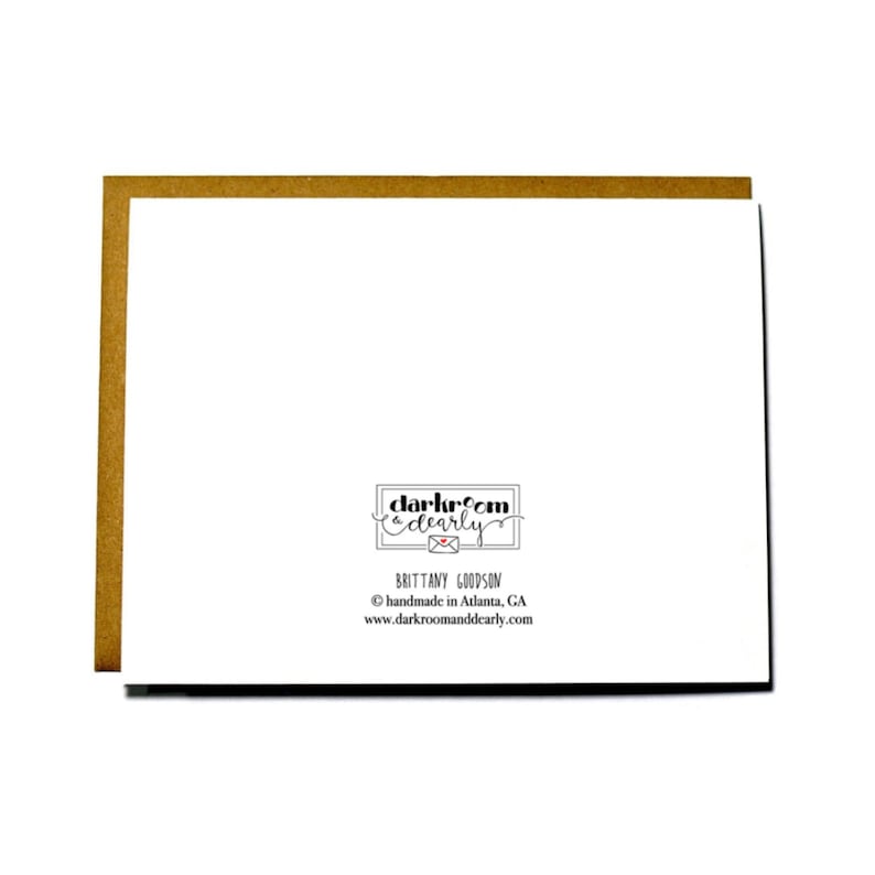 May include: A white card with black text that reads "darkroom & dearly" with a small red heart and the text "BRITTANY GOODSON" below. The text "handmade in Atlanta, GA" and "www.darkroomanddearly.com" are also included in black text.