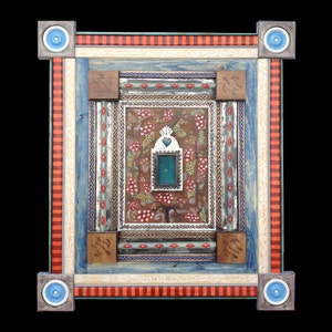 May include: A colorful framed artwork with a central design featuring a small window with a teal blue pane. The frame is made of wood and has multiple layers of painted details in red, blue, white, and brown.