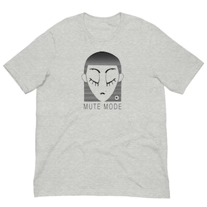 Op de afbeelding: Een lichtgrijs gemêleerd T-shirt met korte mouwen en een zwarte afbeelding van een gestileerd gezicht met gesloten ogen en lange wimpers. Onder het gezicht staat de tekst MUTE MODE in zwarte hoofdletters, vergezeld van een klein luidsprekericoon.