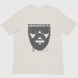 Könnte beinhalten: Ein hellbeiges Kurzarm-T-Shirt mit einem dunkelgrauen Grafikdruck auf der Brust. Das Design zeigt das Wort BARCODE über einer stilisierten Gesichtsform aus vertikalen Linien, die in der Mitte des Bartbereichs ein Pik-Symbol integriert.