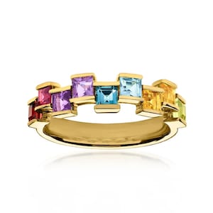 Può includere: Un anello in oro con una serie di pietre preziose a taglio quadrato in uno spettro arcobaleno, tra cui pietre rosse, viola, blu, gialle e verdi. Le pietre sono incastonate in montature d'oro individuali disposte a gradini sfalsati.