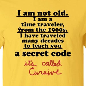 May include: A bright yellow short-sleeved t-shirt featuring black text that reads: I am not old. I am a time traveler, from the 1900s. I have traveled many decades to teach you a secret code. Below this, red cursive text reads: it's called Cursive.