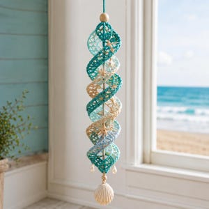 May include: A hanging spiral wind spinner crafted from crocheted yarn in shades of teal, light blue, and cream. The structure features small starfish accents attached to the spiral, a wooden bead at the top, and a large white seashell at the bottom.