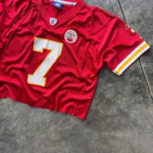 May include: A cropped red football jersey with the number 7 in white and a yellow outline. The jersey has a V-neck and white and yellow stripes on the sleeves. A team logo is visible on the chest.