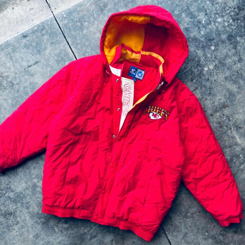 May include: Red and yellow hooded puffer jacket with the Kansas City Chiefs logo and "Chiefs" written vertically on the zipper.