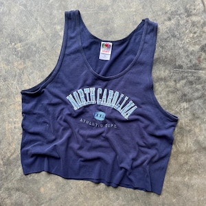 May include: Navy blue tank top with the words "North Carolina" in light blue arched across the chest. Below the text is "XXL" inside a circle and "ATHLETIC DEPT." The tank top is a Fruit of the Loom Heavy XL.