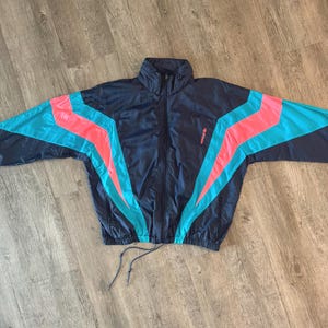 May include: A navy blue vintage track jacket with a full zip and a high collar. The jacket has bright pink and teal stripes across the sleeves and shoulders. The Adidas logo is visible on the right chest.