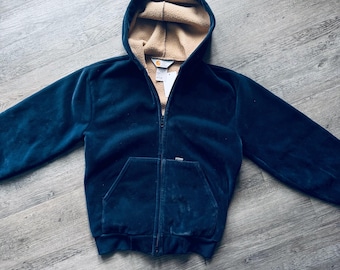May include: A navy blue hooded zip-up jacket with a tan-colored fleece lining. The jacket has a front pocket and a tag attached to the zipper. The jacket is made of a soft, velvety material.
