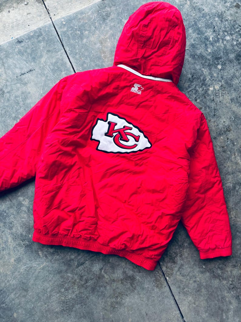 May include: Red Starter brand hooded jacket with a white and red Kansas City Chiefs logo on the back.