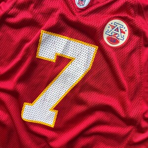 May include: Red mesh football jersey with the number 7 in white with a yellow outline. Features a team logo patch and an NFL Equipment tag. The jersey is a vibrant red.