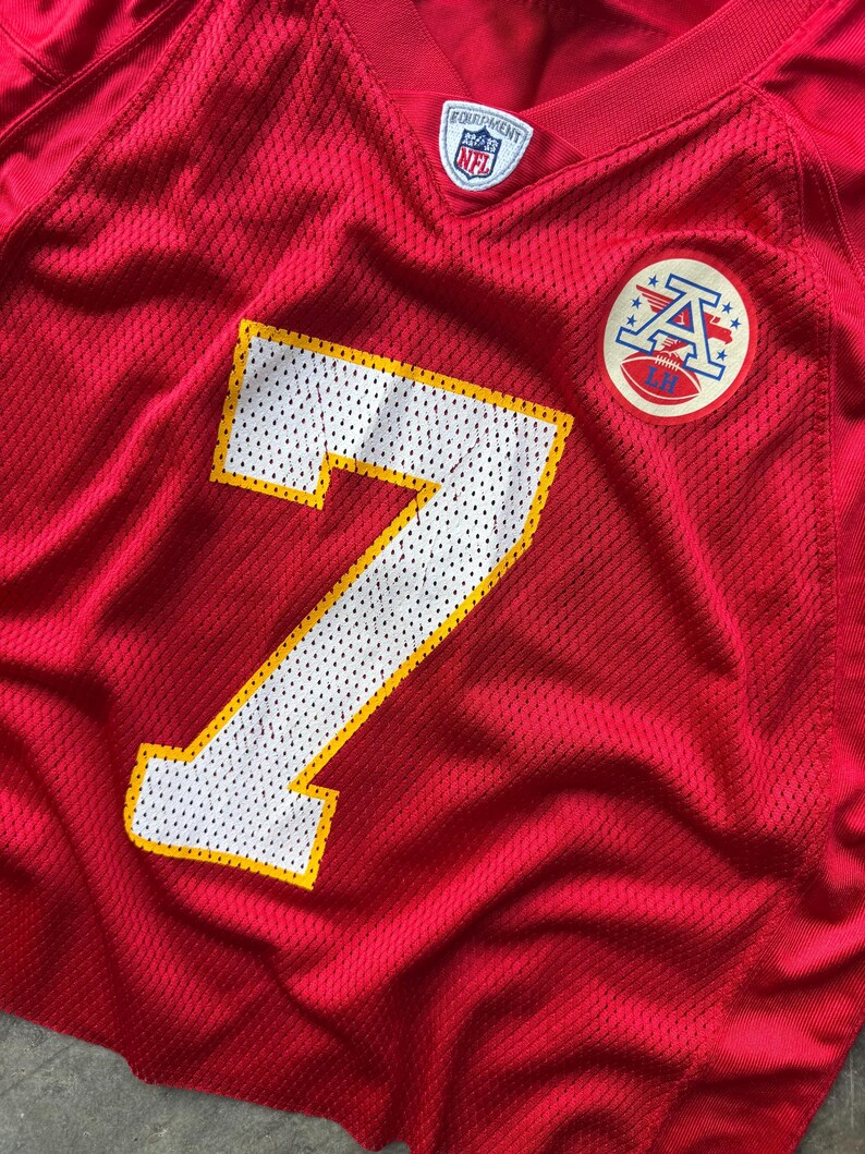 May include: Red mesh football jersey with the number 7 in white with a yellow outline. Features a team logo patch and an NFL Equipment tag. The jersey is a vibrant red.