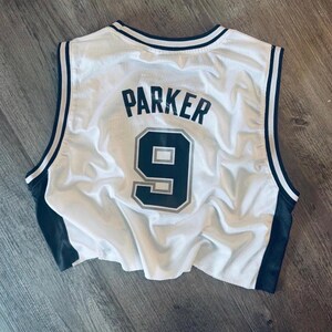Puede incluir: Una camiseta de baloncesto sin mangas de malla blanca con ribetes negros en el cuello y las sisas. La parte posterior muestra el nombre PARKER en letras negras sobre el n&uacute;mero 9, impreso en negro con un contorno gris sobre la tela.