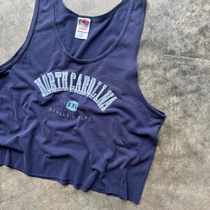 May include: Navy blue tank top with the words "NORTH CAROLINA" in light blue lettering. The text "XXL" is below the main text, and "ATHLETIC DEPT." is printed below that. The tank top is made of a soft material.