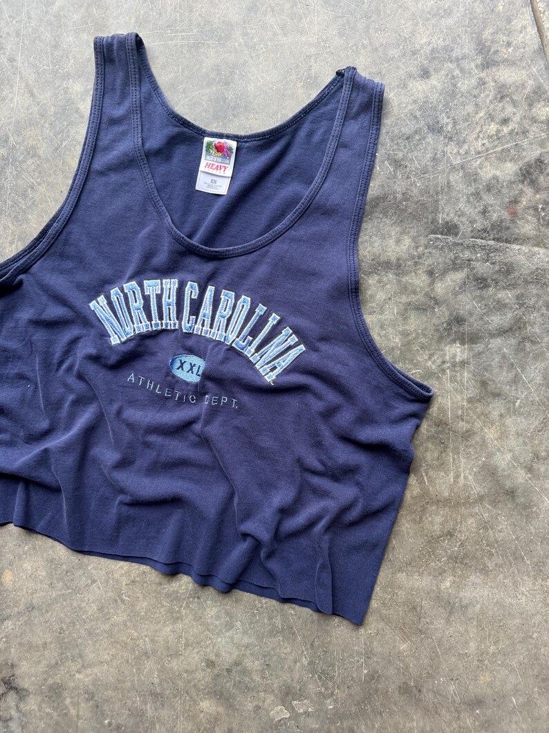 May include: Navy blue tank top with the words "NORTH CAROLINA" in light blue lettering. The text "XXL" is below the main text, and "ATHLETIC DEPT." is printed below that. The tank top is made of a soft material.