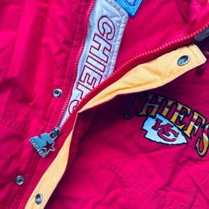 May include: Red and yellow Starter brand jacket with the Kansas City Chiefs logo and "Chiefs" written on the front. The jacket has a zipper and a snap closure.