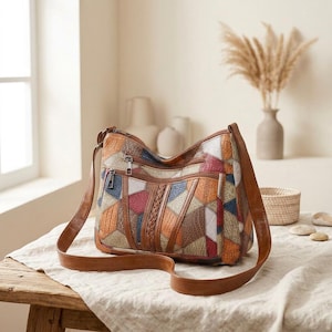 May include: A multi-colored patchwork shoulder bag featuring a textured geometric pattern in shades of brown, orange, blue, and cream. The bag includes a brown leather-like strap, two front zippered pockets, and a braided vertical accent detail.