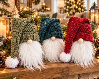 May include: Three decorative gnomes featuring long white faux fur beards and wooden bead noses. Each gnome wears a tall, textured, crocheted hat in olive green, dark teal, or deep red, topped with a fluffy white pom-pom at the end of the hat.