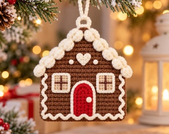 May include: A brown crochet gingerbread house ornament featuring a red door, two windows with brown cross-stitching, a white heart detail, and white scalloped trim along the roof and base, suspended by a matching white yarn loop.