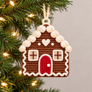 Puede incluir: Un adorno de casa de jengibre de ganchillo marr&oacute;n con puerta roja, ribetes blancos estilo glaseado, dos ventanas con detalles de punto de cruz y un peque&ntilde;o coraz&oacute;n blanco sobre la puerta. Incluye un lazo para colgar.