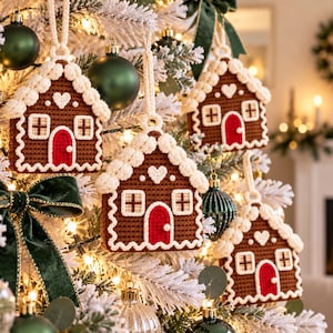 Puede incluir: Cuatro adornos de casas de jengibre hechos a ganchillo colgados en un &aacute;rbol de Navidad. Cada casa marr&oacute;n tiene una puerta roja arqueada, marcos de ventanas blancos, un detalle de coraz&oacute;n blanco y un borde blanco texturizado.