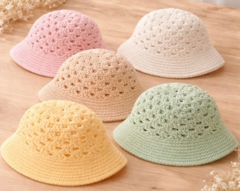 May include: A collection of five crochet bucket hats in pastel colours including light pink, cream, beige, yellow, and light green. Each hat features a consistent open-work stitch pattern on the crown and a solid, tightly crocheted brim.