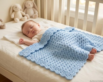 Puede incluir: Una manta de bebé tejida a ganchillo en color azul claro con un borde festoneado y un patrón de puntos texturizado. La manta cubre a un bebé dormido que lleva un body blanco de manga corta, sobre una sábana blanca en una cuna.