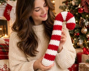 May include: A crochet candy cane decoration featuring alternating horizontal stripes of bright red and white yarn. The candy cane has a curved top and a soft, textured appearance, crafted with a thick yarn stitch pattern throughout the entire piece.