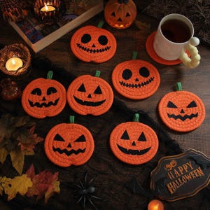 Puede incluir: Un juego de siete posavasos redondos de tela naranja con forma de calabazas de Halloween, con rasgos faciales negros cosidos y tallos verdes. Cada posavasos muestra una expresión de calabaza diferente sobre un fondo oscuro.