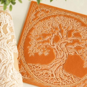 May include: A cylindrical beige patterned rolling pin and a square orange flat stamp, both featuring an embossed design of a tree with intricate roots and branches enclosed within a circular border and decorative corner elements.