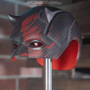 May include: A full-head helmet featuring two prominent horns on the top, a textured black and red exterior pattern, and dark red eye lenses. The interior lining is bright red, and the text MIGRAN STUDIO.com is visible above the helmet.