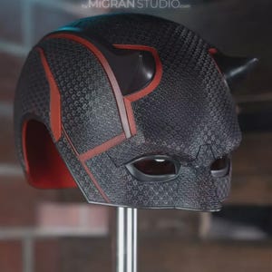 May include: A black helmet with a textured surface and red accents, featuring two prominent horns on the top and eye openings. The text "by MIGRAN STUDIO.com" is visible at the top. The interior of the helmet is lined with red material.