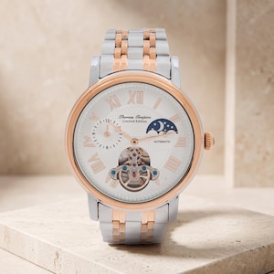 May include: A Thomas Tompion Limited Edition automatic wristwatch with a white dial, rose gold Roman numerals, and a moon phase indicator. The watch features a visible balance wheel, a rose gold bezel, and a two-tone silver and rose gold metal link bracelet.