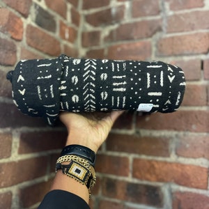 May include: Black and white patterned fabric rolled up and held in a hand. The fabric has a geometric design with white lines and dots on a black background. The hand is wearing a black watch and gold bracelets.