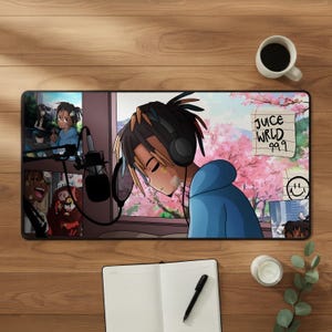 Puede incluir: Una alfombrilla de escritorio rectangular con una ilustración estilo anime de una persona con rastas que lleva auriculares y una sudadera azul. El diseño incluye un micrófono, cerezos en flor y una nota con el texto JUICE WRLD 999.