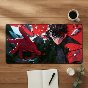 Può includere: Un tappetino da scrivania rettangolare con un'illustrazione grafica di un personaggio dai capelli scuri che indossa una maschera bianca e un cappotto nero, che protende una mano guantata di rosso su uno sfondo rosso vivace con frammenti.