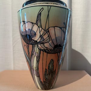 Könnte beinhalten: Eine konisch geformte Keramikvase mit handgemaltem Blumenmotiv und schwarzen Umrandungen. Die Oberfläche zeigt einen Farbverlauf in sanften Pfirsich- und Salbeigrüntönen, die stilisierte Mohnblumen und Blätter auf einer glatten, glänzenden Glasur darstellen.