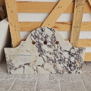 May include: A rectangular marble backsplash with a curved top edge featuring three circular faucet holes. The stone surface displays a prominent white base colour with intricate, dark purple and brown veining patterns throughout the slab.